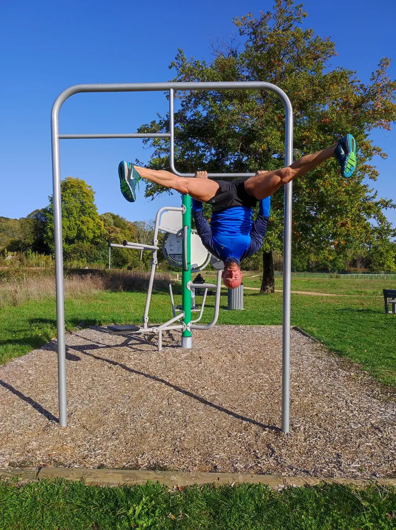Tony en position horizontale sur une barre de street workout, dans un parc par temps clair